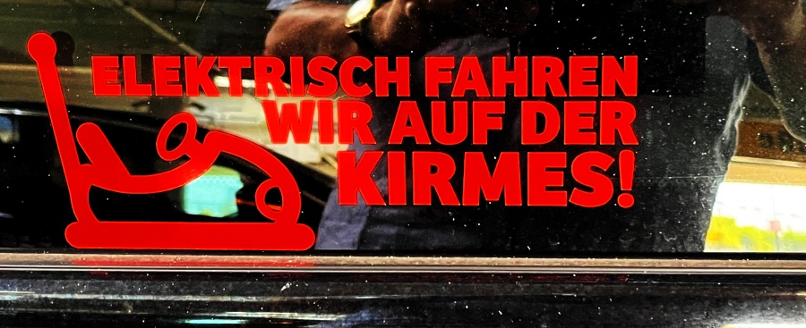 zeigt einen Autoauffkleber an Autofenster mit dem Text: Elektrisch fahren wir auf der Kirmes